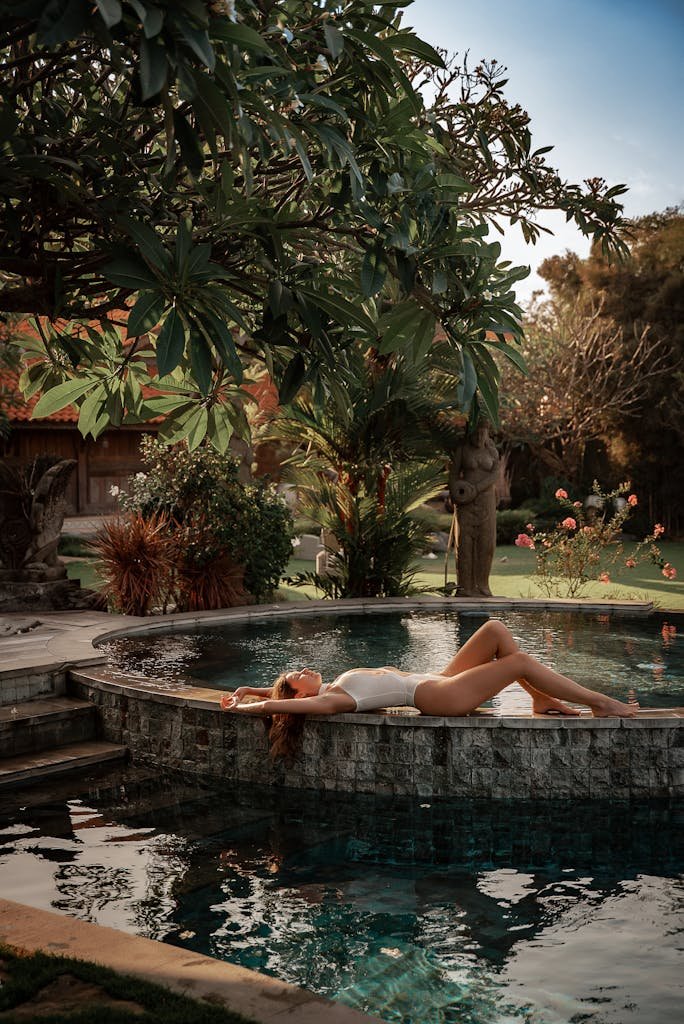 Woman in swimsuit lounging by a peaceful garden pool, surrounded by lush greenery and tranquil scenery.